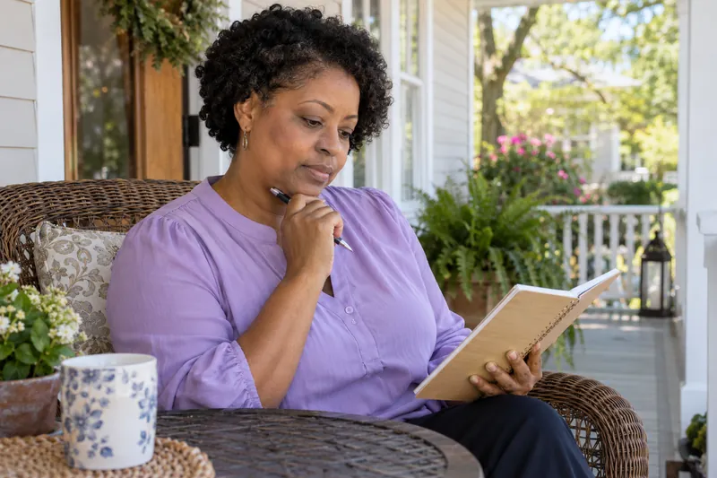 A visitor checking a local opening-hours note in a notebook on a sunny front porch