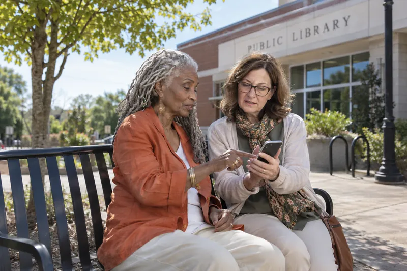 A visitor asking a companion for directions while pointing at a phone map near a public bench