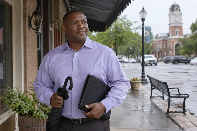 A visitor standing under a storefront awning with a closed umbrella and appointment folder