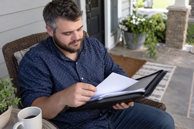 A visitor looking through a document pouch on a home porch before a planned appointment