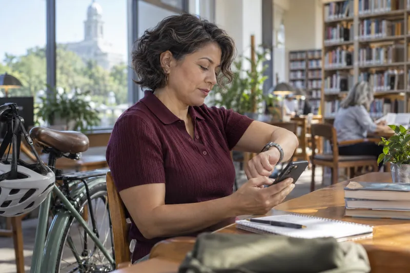 A visitor checking a watch and a phone beside a parked bicycle before a daytime appointment