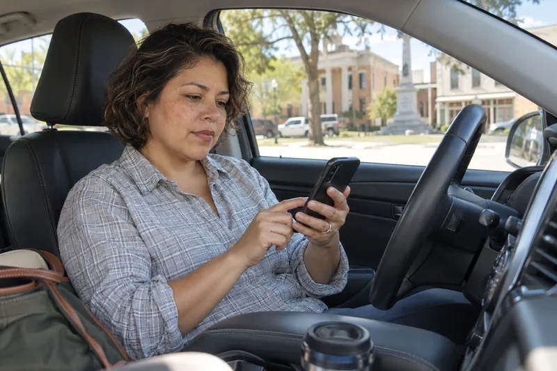 A visitor sitting in a parked car checking a phone route before setting off, car stationary