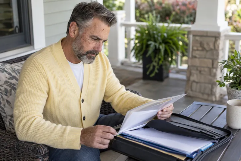 A visitor looking through a document pouch on a home porch before a planned appointment