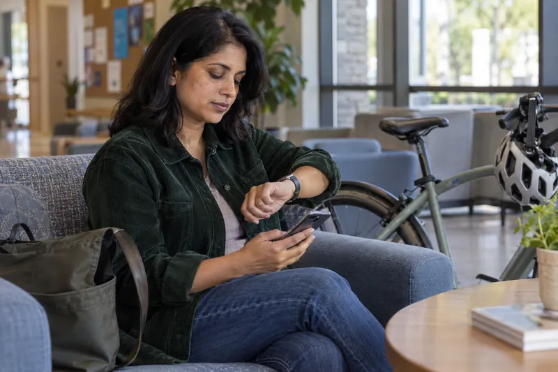 A visitor checking a watch and a phone beside a parked bicycle before a daytime appointment